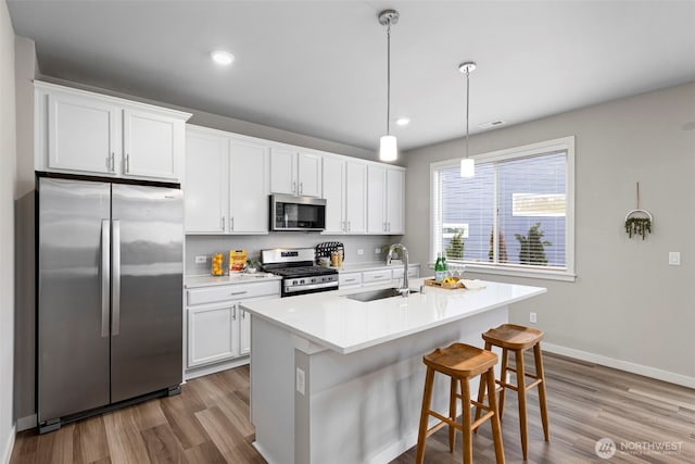 kitchen featuring a sink, white cabinets, light countertops, appliances with stainless steel finishes, and decorative light fixtures