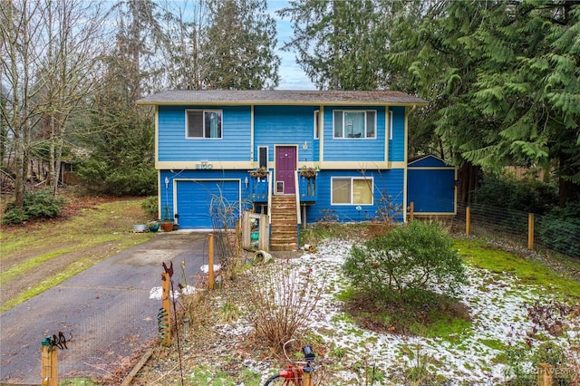 bi-level home with a garage, driveway, and fence