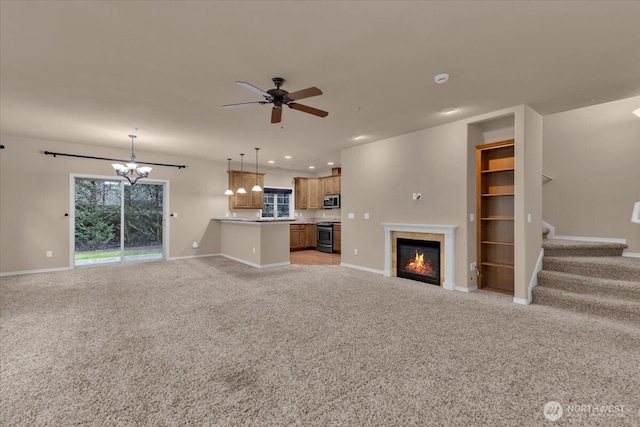 unfurnished living room featuring baseboards, a tiled fireplace, light colored carpet, stairs, and ceiling fan with notable chandelier