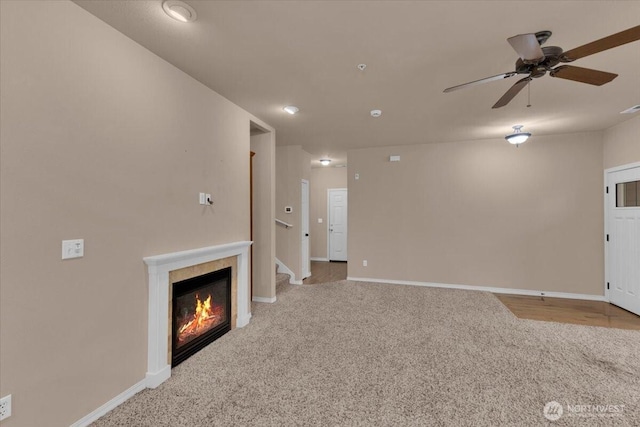 unfurnished living room with carpet, a glass covered fireplace, stairway, and baseboards