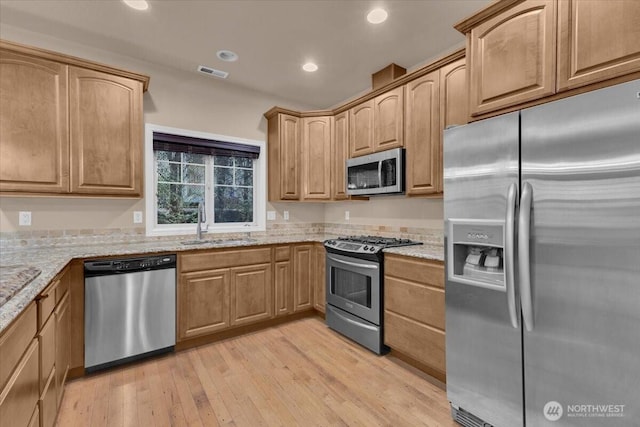 kitchen with light stone counters, light wood-style flooring, a sink, visible vents, and appliances with stainless steel finishes