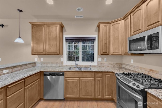 kitchen featuring visible vents, light wood-style flooring, light stone counters, stainless steel appliances, and a sink