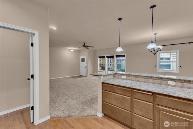 kitchen with a ceiling fan, hanging light fixtures, light wood-style flooring, and light stone countertops