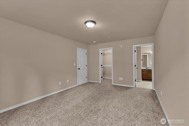 unfurnished bedroom with a walk in closet, a closet, light carpet, and baseboards