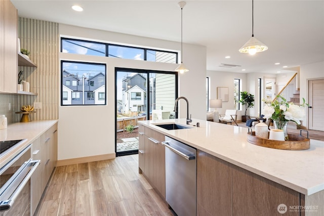 kitchen featuring hanging light fixtures, appliances with stainless steel finishes, a kitchen island with sink, a sink, and modern cabinets