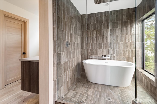 full bath featuring a soaking tub, a tile shower, and tile walls