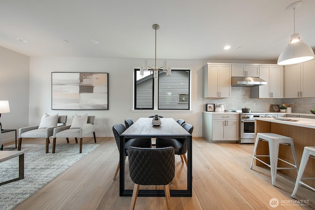 kitchen with tasteful backsplash, hanging light fixtures, high end stainless steel range oven, light countertops, and under cabinet range hood