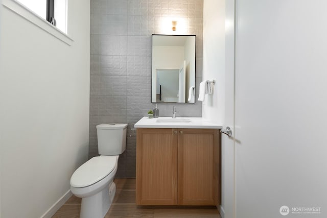 half bathroom featuring toilet, wood finished floors, vanity, tile walls, and baseboards