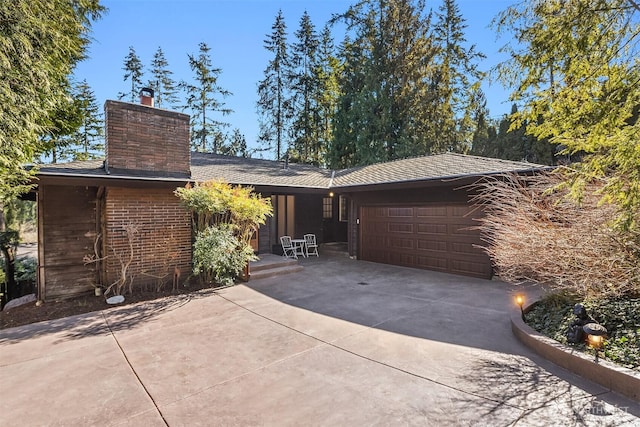 view of front of house with concrete driveway, brick siding, a chimney, and an attached garage