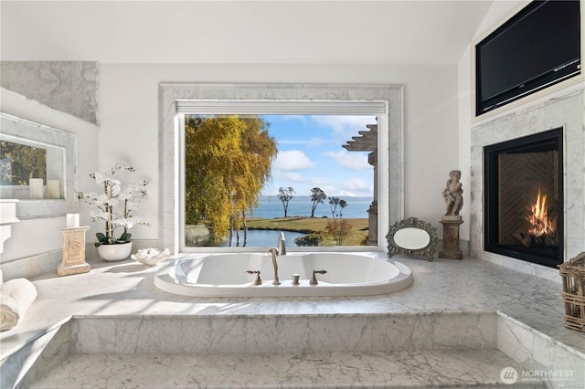 bathroom with a water view, a fireplace, and a tub with marble appearance