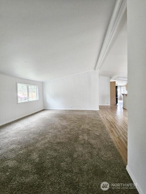 empty room with carpet flooring, beam ceiling, and baseboards