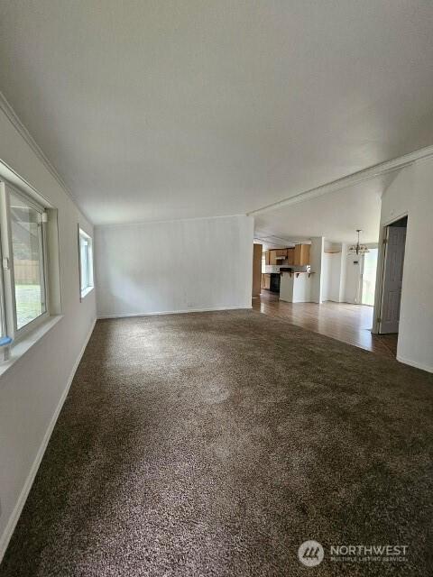 unfurnished living room featuring ornamental molding, dark colored carpet, and baseboards