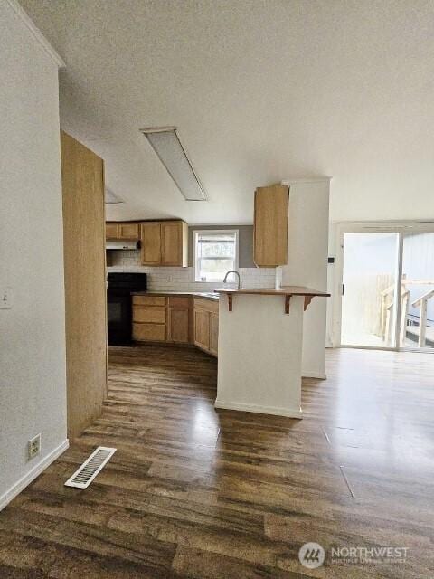 kitchen featuring dark wood finished floors, light countertops, visible vents, range, and a kitchen bar