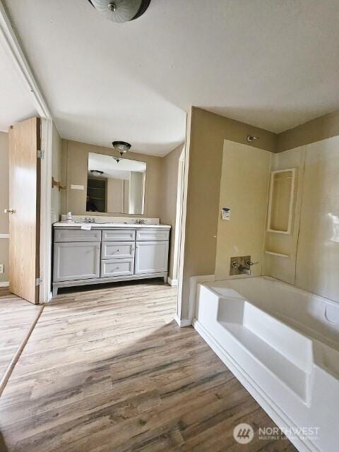 full bath with double vanity, baseboards, wood finished floors, and a bath