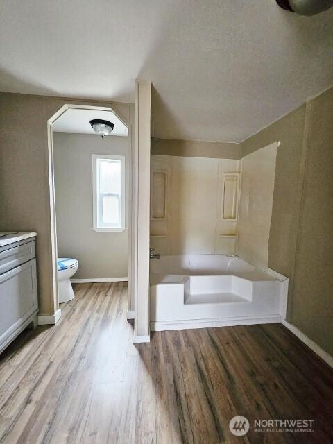 full bath featuring bathtub / shower combination, toilet, wood finished floors, vanity, and baseboards