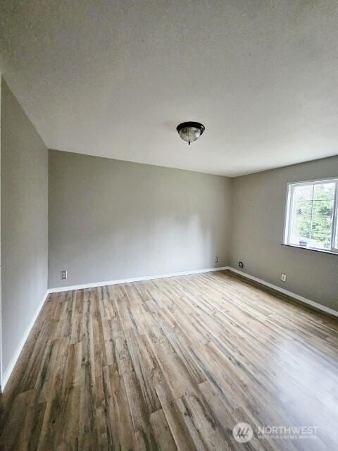 spare room featuring a textured ceiling, light wood-type flooring, and baseboards