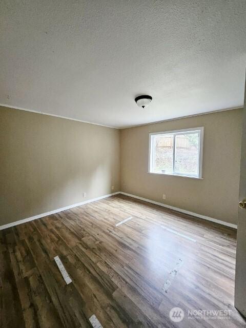 spare room featuring a textured ceiling, wood finished floors, and baseboards