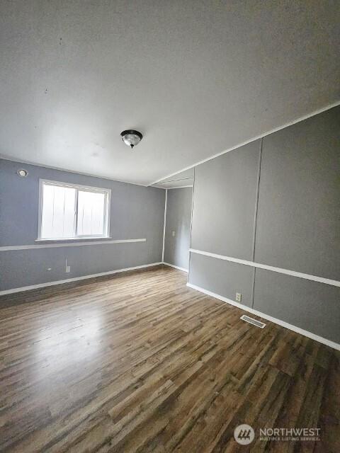 empty room with dark wood-style floors, visible vents, and baseboards