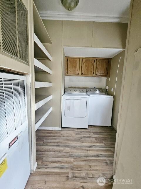 clothes washing area with light wood finished floors, a heating unit, separate washer and dryer, and crown molding