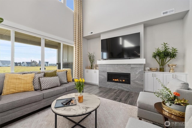 living room with a tile fireplace, visible vents, a towering ceiling, and wood finished floors