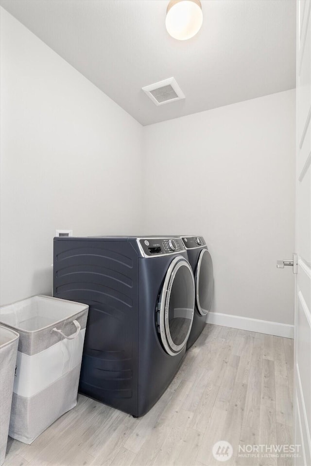 clothes washing area with light wood-style flooring, laundry area, visible vents, baseboards, and washer and clothes dryer