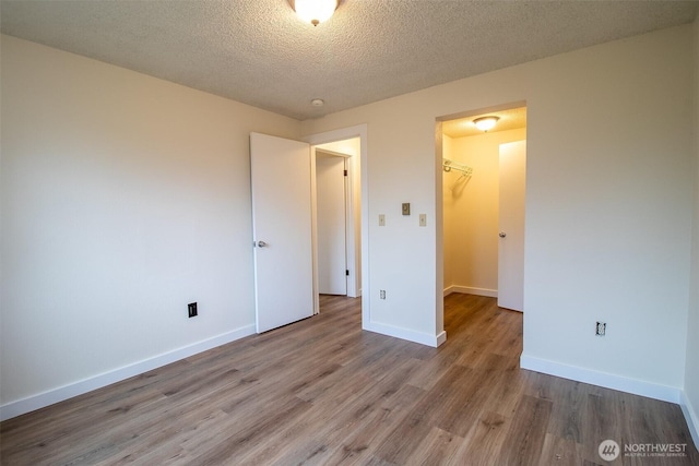 unfurnished bedroom with a textured ceiling, a spacious closet, baseboards, and wood finished floors