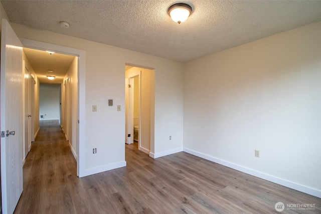 unfurnished bedroom with a textured ceiling, wood finished floors, and baseboards