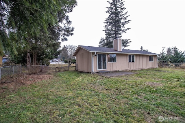 back of house with board and batten siding, fence private yard, a chimney, and a lawn