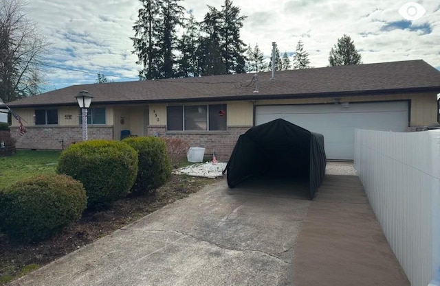 single story home featuring a garage, driveway, brick siding, and fence