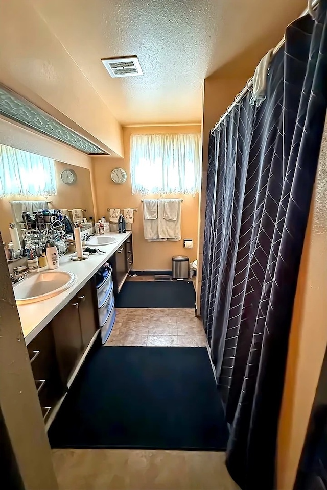 full bathroom featuring visible vents, a sink, a textured ceiling, and double vanity