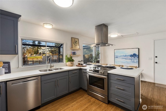 kitchen with island range hood, stainless steel appliances, a peninsula, a sink, and gray cabinets