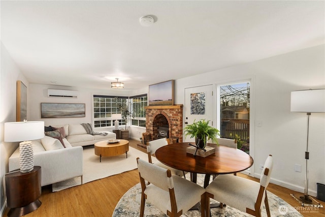 living room featuring baseboards, light wood finished floors, a wall mounted air conditioner, and a brick fireplace