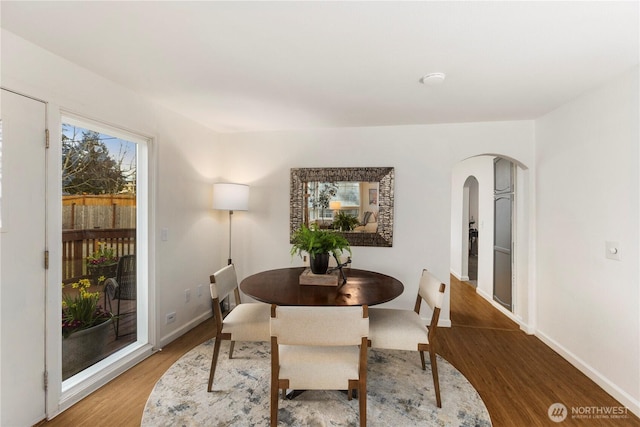 dining space with arched walkways, wood finished floors, and baseboards