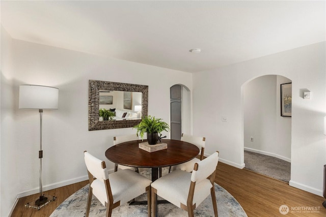 dining area with arched walkways, wood finished floors, and baseboards