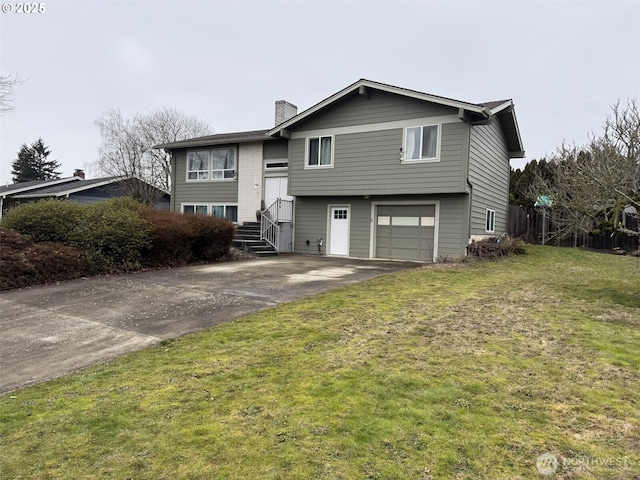 bi-level home with an attached garage, a front yard, a chimney, and driveway