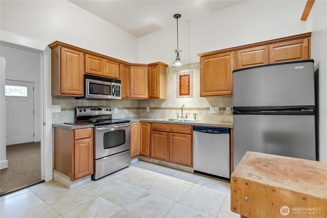 kitchen with brown cabinetry, appliances with stainless steel finishes, hanging light fixtures, light countertops, and a sink