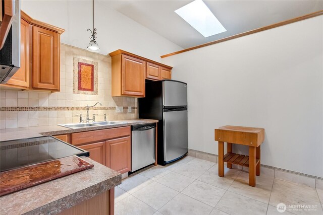 kitchen featuring stainless steel appliances, a skylight, a sink, decorative backsplash, and decorative light fixtures