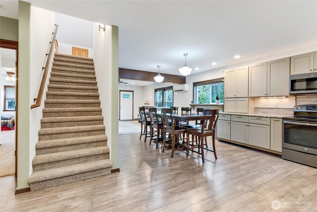 kitchen with light wood-style flooring, gray cabinetry, stainless steel appliances, a wall mounted air conditioner, and pendant lighting