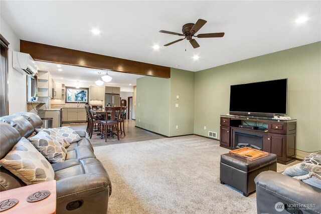 living room with visible vents, a wall unit AC, light carpet, and baseboards