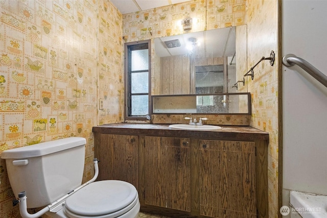 bathroom with vanity, toilet, and wallpapered walls