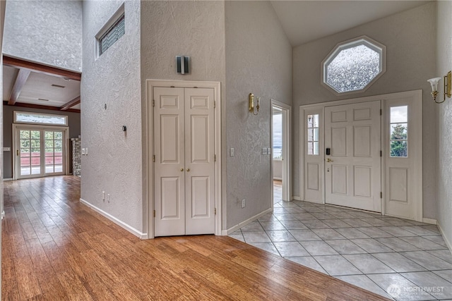 entryway featuring a towering ceiling, light wood-style flooring, baseboards, and a textured wall