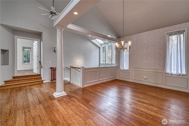 unfurnished dining area featuring lofted ceiling, a wainscoted wall, wood finished floors, and ornate columns