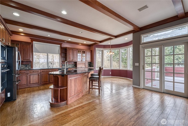 kitchen featuring glass insert cabinets, a kitchen island with sink, brown cabinetry, and open shelves