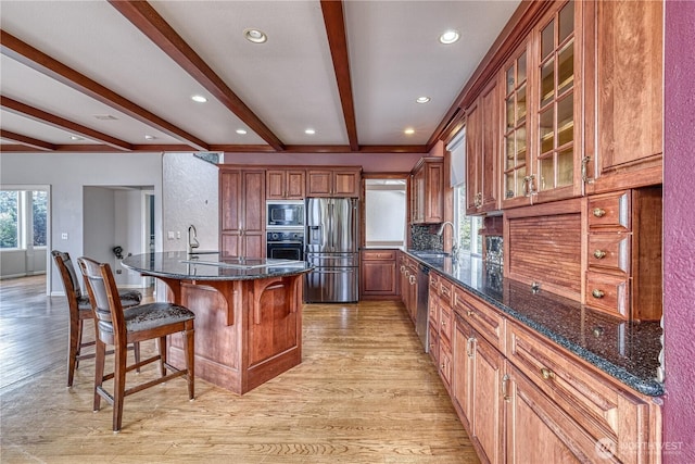 kitchen featuring light wood-style flooring, a sink, appliances with stainless steel finishes, dark stone counters, and glass insert cabinets