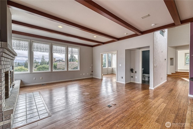 unfurnished living room featuring a fireplace, visible vents, light wood-style floors, beamed ceiling, and baseboards