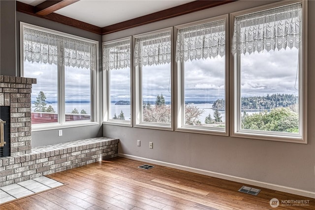 unfurnished sunroom featuring a brick fireplace, visible vents, and a water view