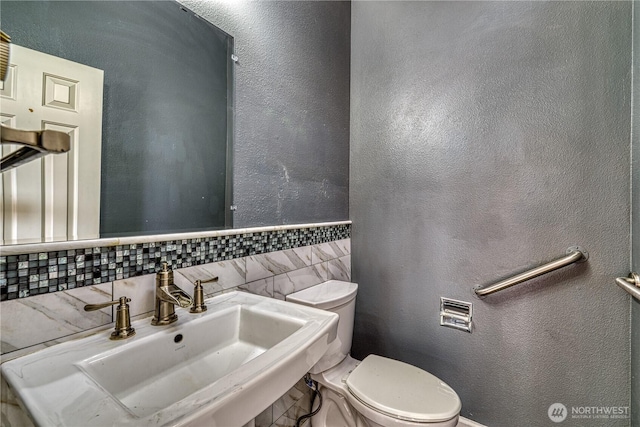 bathroom featuring tasteful backsplash, a textured wall, a sink, and toilet