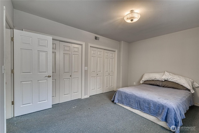 bedroom with multiple closets, visible vents, and dark carpet