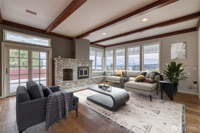 living area with a fireplace, visible vents, light wood-type flooring, beamed ceiling, and baseboards