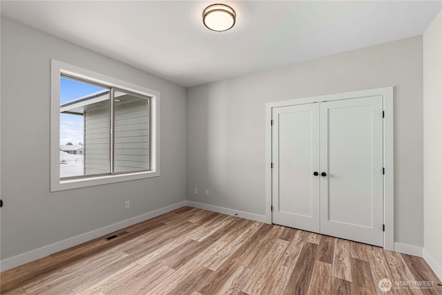 unfurnished bedroom featuring light wood finished floors, visible vents, baseboards, and a closet